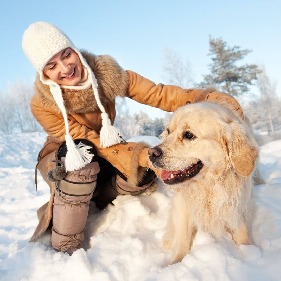 Woman with a bobble hat on with her pet dog in the snow